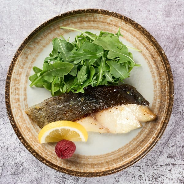 Grilled fish with crispy skin, a side of fresh arugula, lemon, and a red berry on a rustic plate.