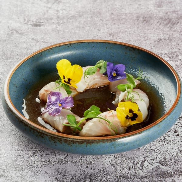 KEI's delicate Japanese dish with white fish, edible flowers, and microgreens in a blue bowl.