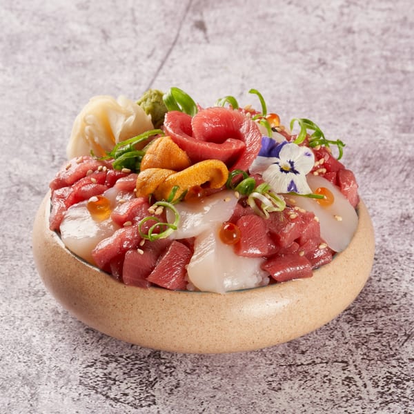 A colorful Japanese chirashi bowl with tuna, scallops, uni, roe, ginger, and edible flowers.