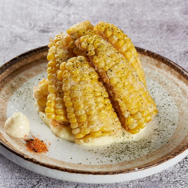 Grilled corn on the cob, seasoned with herbs and spices, served with mayonnaise on a plate.